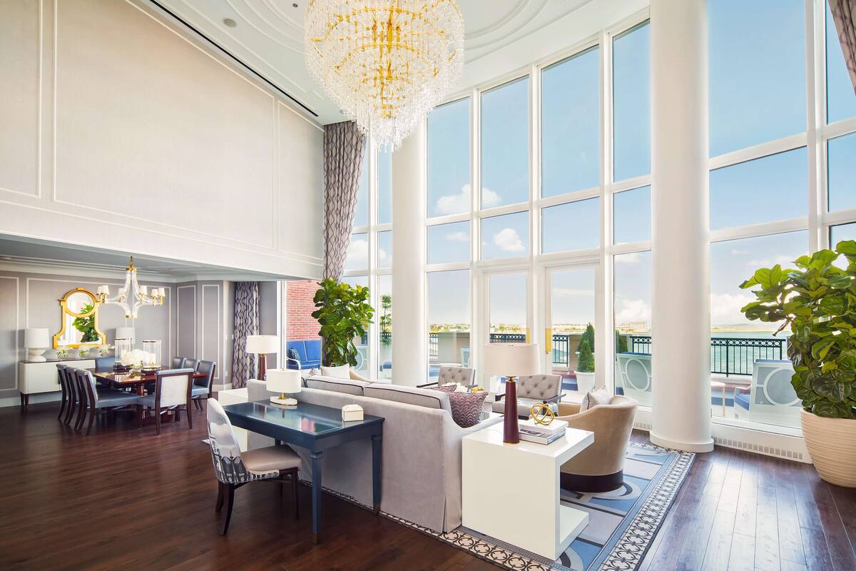 A spacious hotel lobby with a dining area, seating, large windows, and a chandelier.