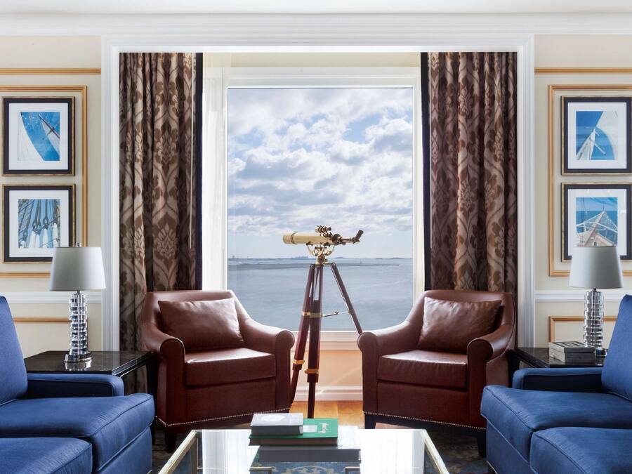 Una habitación con dos sillones de cuero frente a un ventanal con vista al mar. Hay cuadros enmarcados en las paredes y un telescopio sobre trípode en el centro.