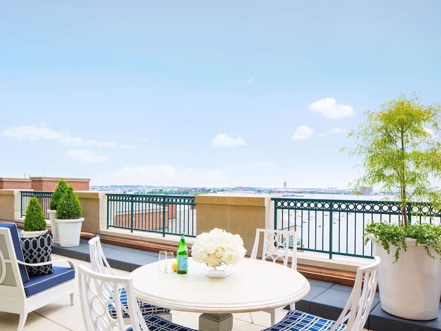 A terrace with a round table, chairs, potted plants, and a view of the city.