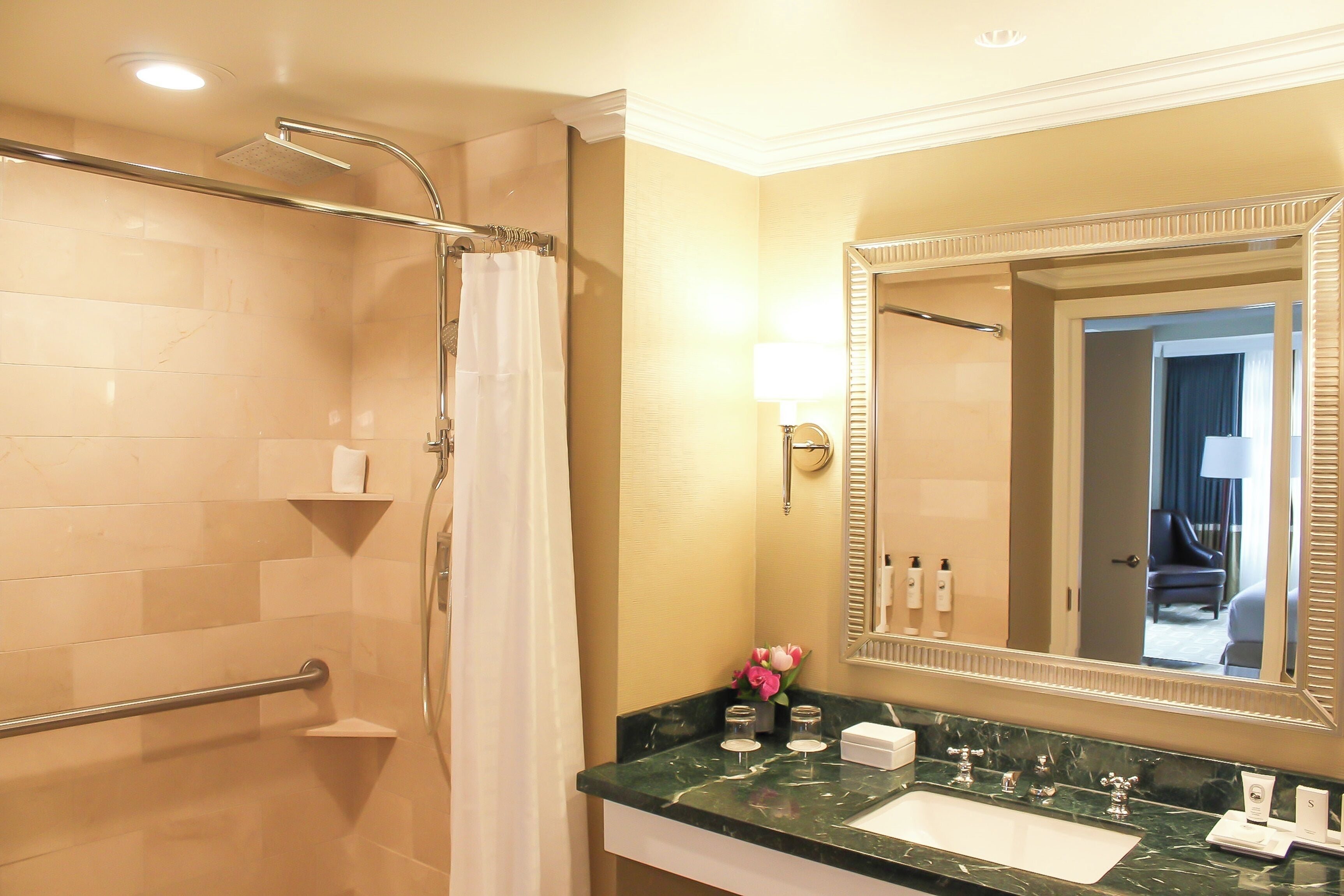 A bathroom with a shower, a sink, a mirror, and a towel rack.