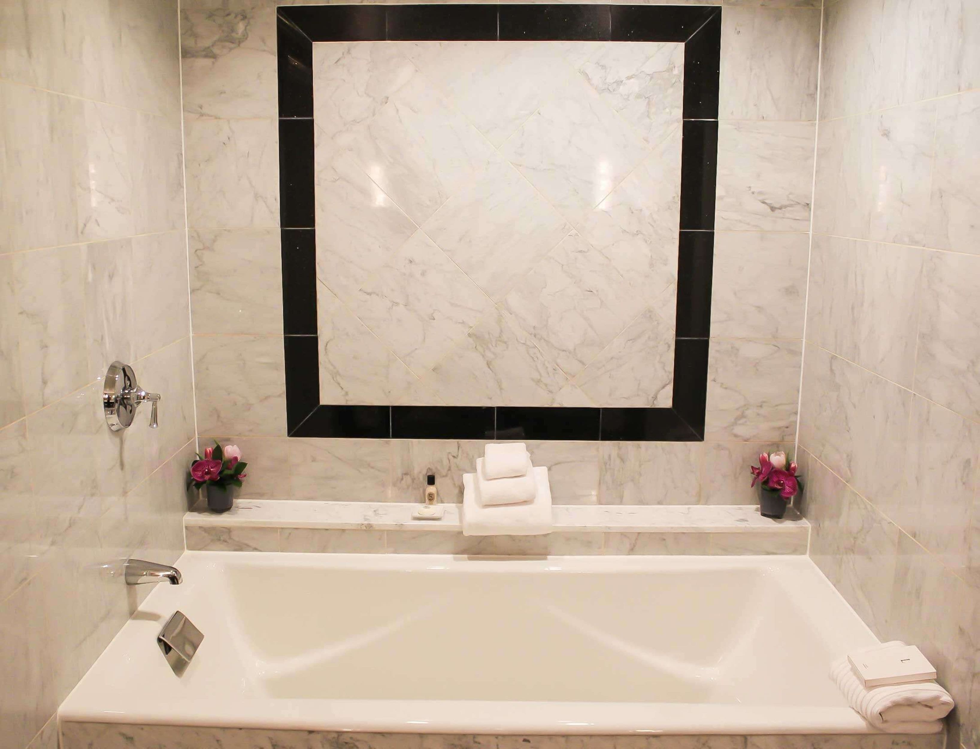 A bathroom with a large mirror, a bathtub, and two flower arrangements.