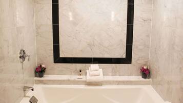 A bathroom with a large mirror, a bathtub, and two flower arrangements.
