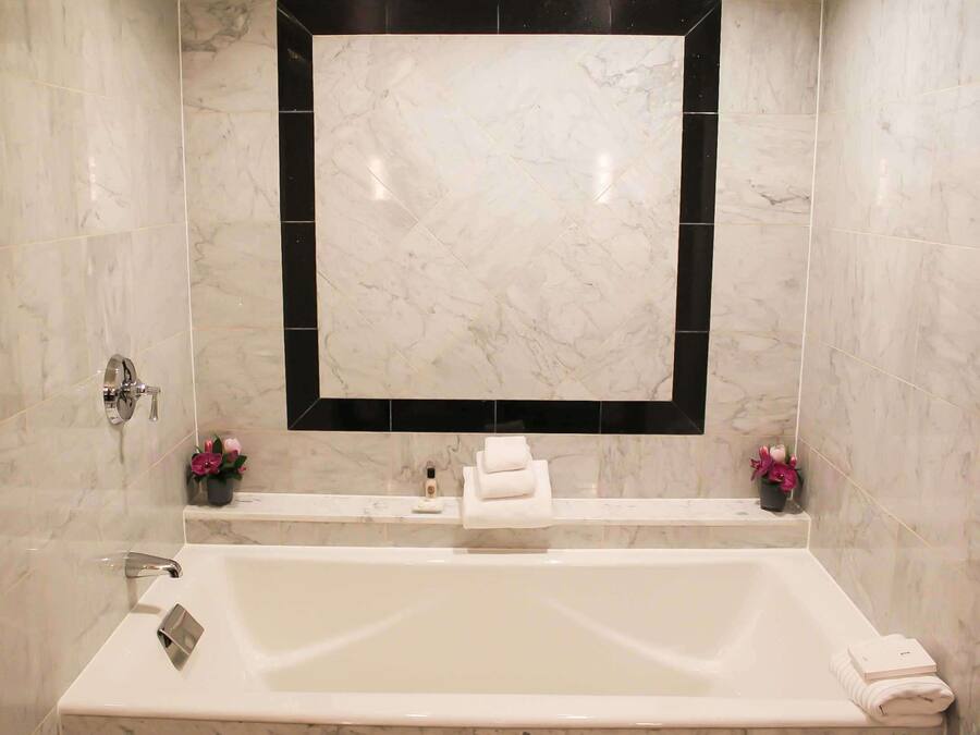 A bathroom with a large mirror, a bathtub, and two flower arrangements.