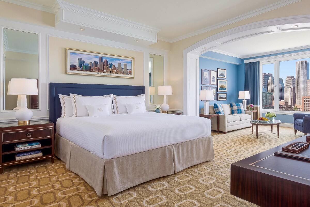 A hotel room with a large bed, a sofa, a desk, and a city view.