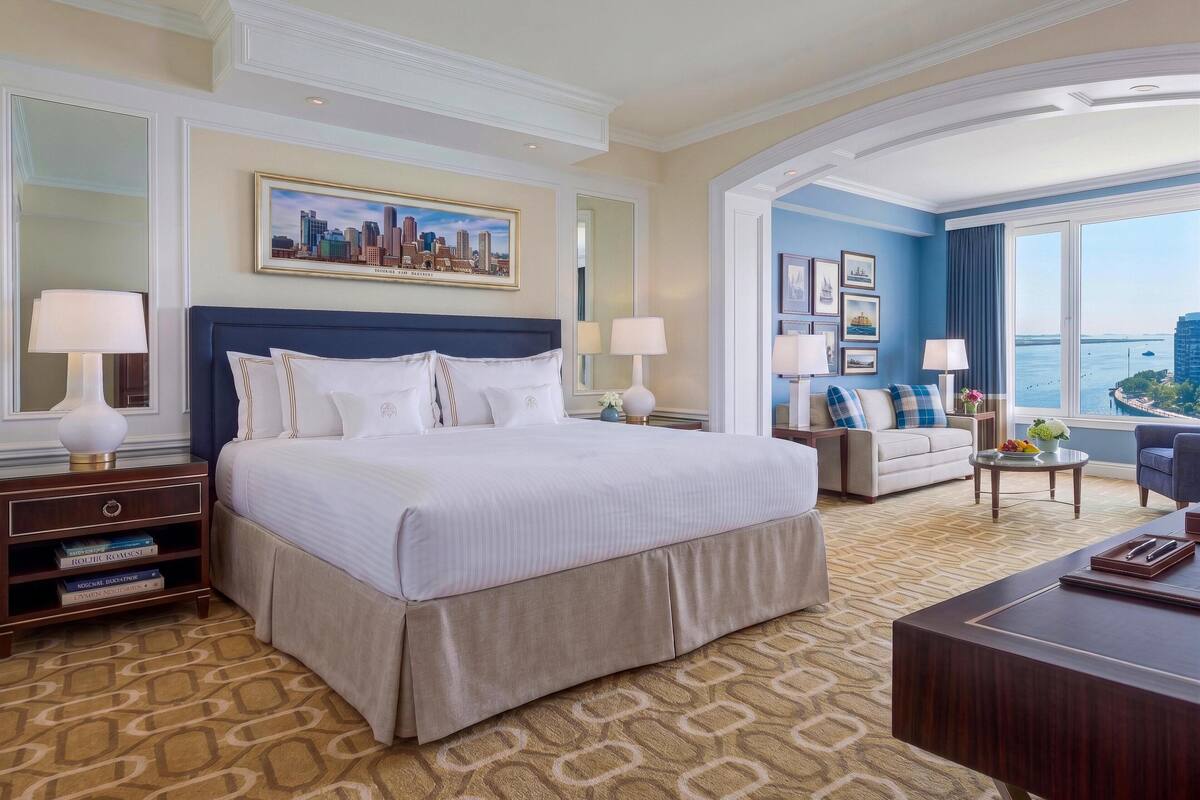 A hotel room with a large bed, a sofa, a desk, and a view of the city.