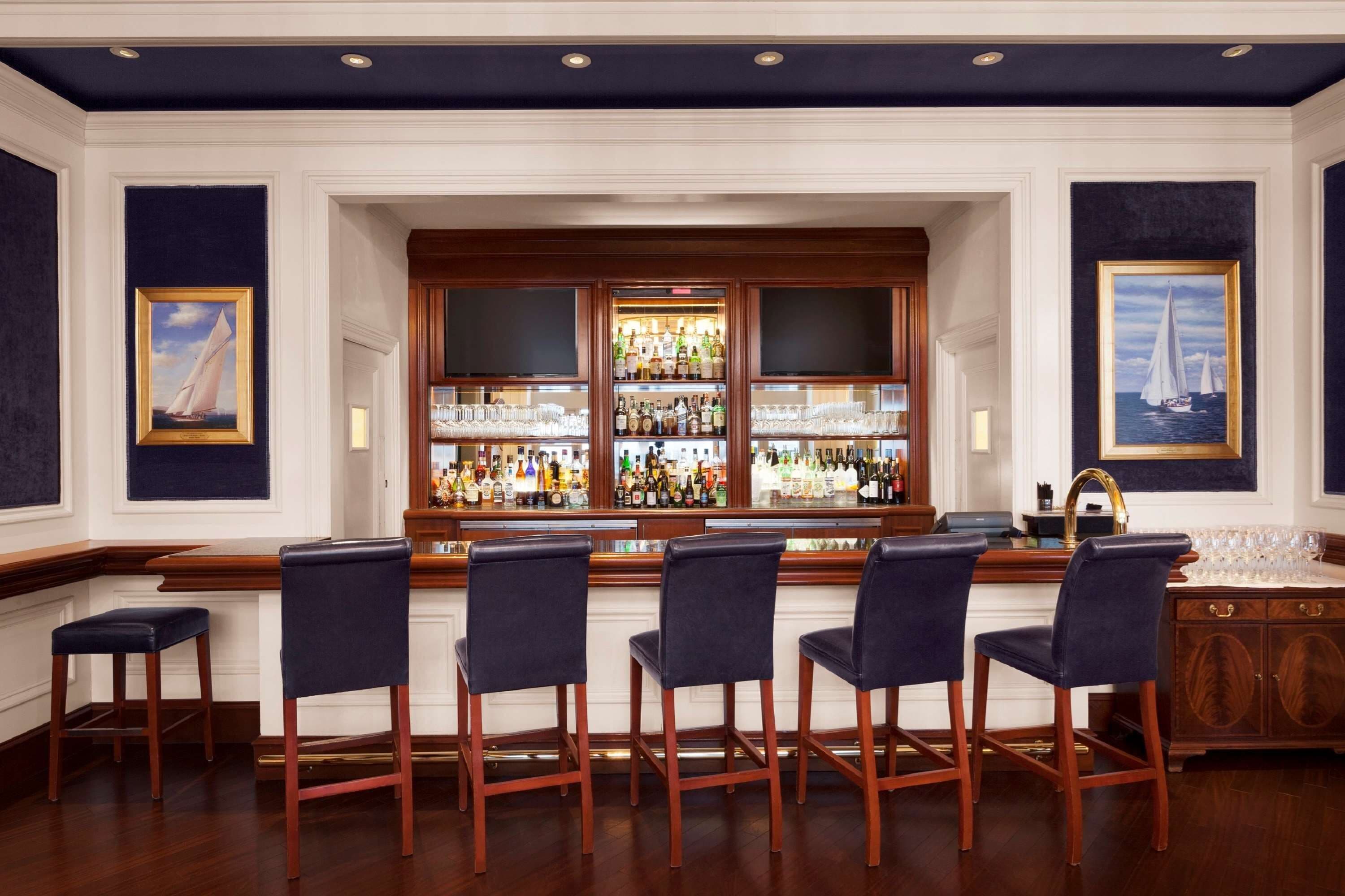 A bar area with wooden bar counters, multiple liquor bottles, and framed maritime paintings.