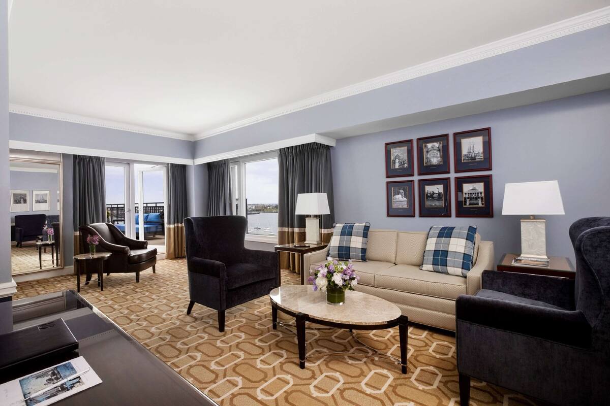A hotel room with a sofa, two armchairs, a coffee table with flowers, a lamp, and framed pictures on the wall.