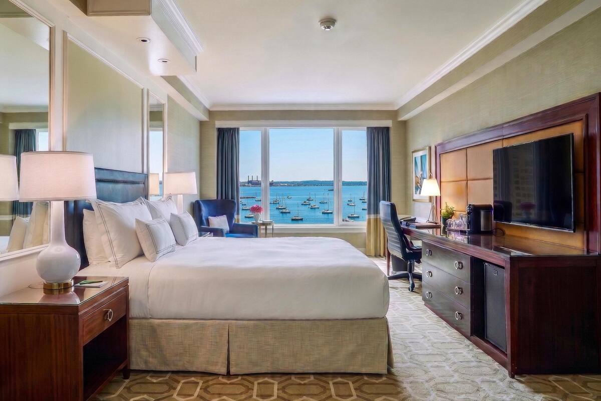 A hotel room with a large bed, a TV, a desk, and a view of the sea.