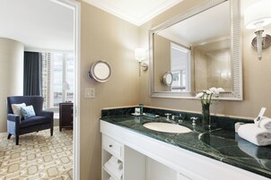 A hotel bathroom with a large mirror, a sink, and a chair.