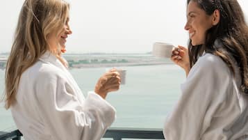 Two individuals in white robes on a balcony with a view of a body of water and distant landscape.