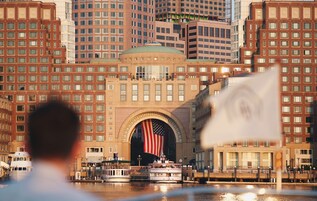 A waterfront building with a large American flag arching over the entrance, surrounded by other high-rise buildings.