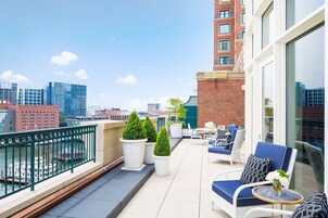 A rooftop terrace with outdoor seating, potted plants, and a view of the city skyline.