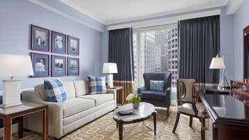 A modern hotel room with a sofa, armchairs, a dining table, and framed pictures on the wall.