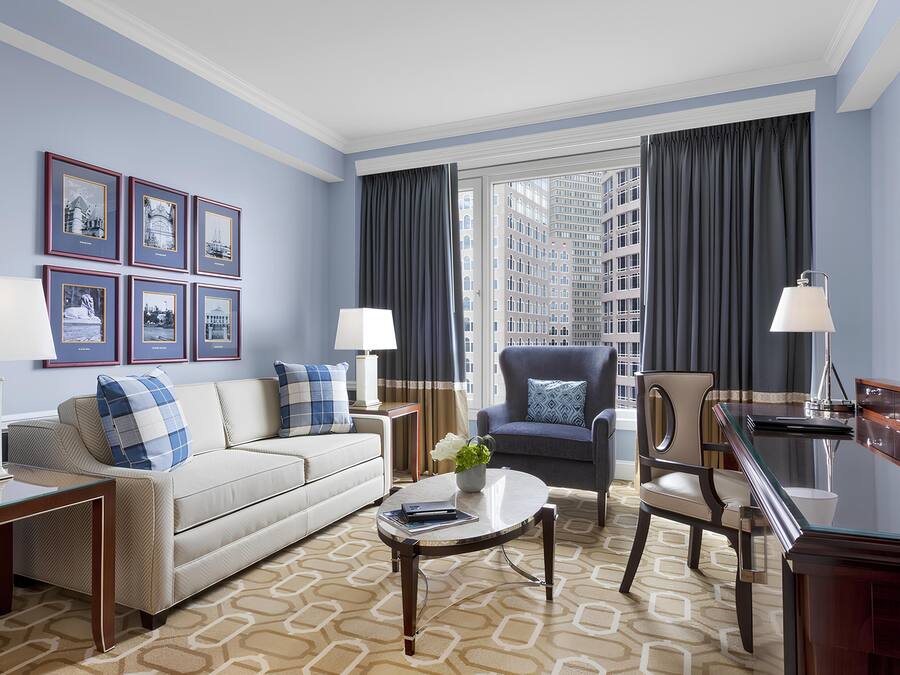 A modern hotel room with a sofa, armchairs, a dining table, and framed pictures on the wall.