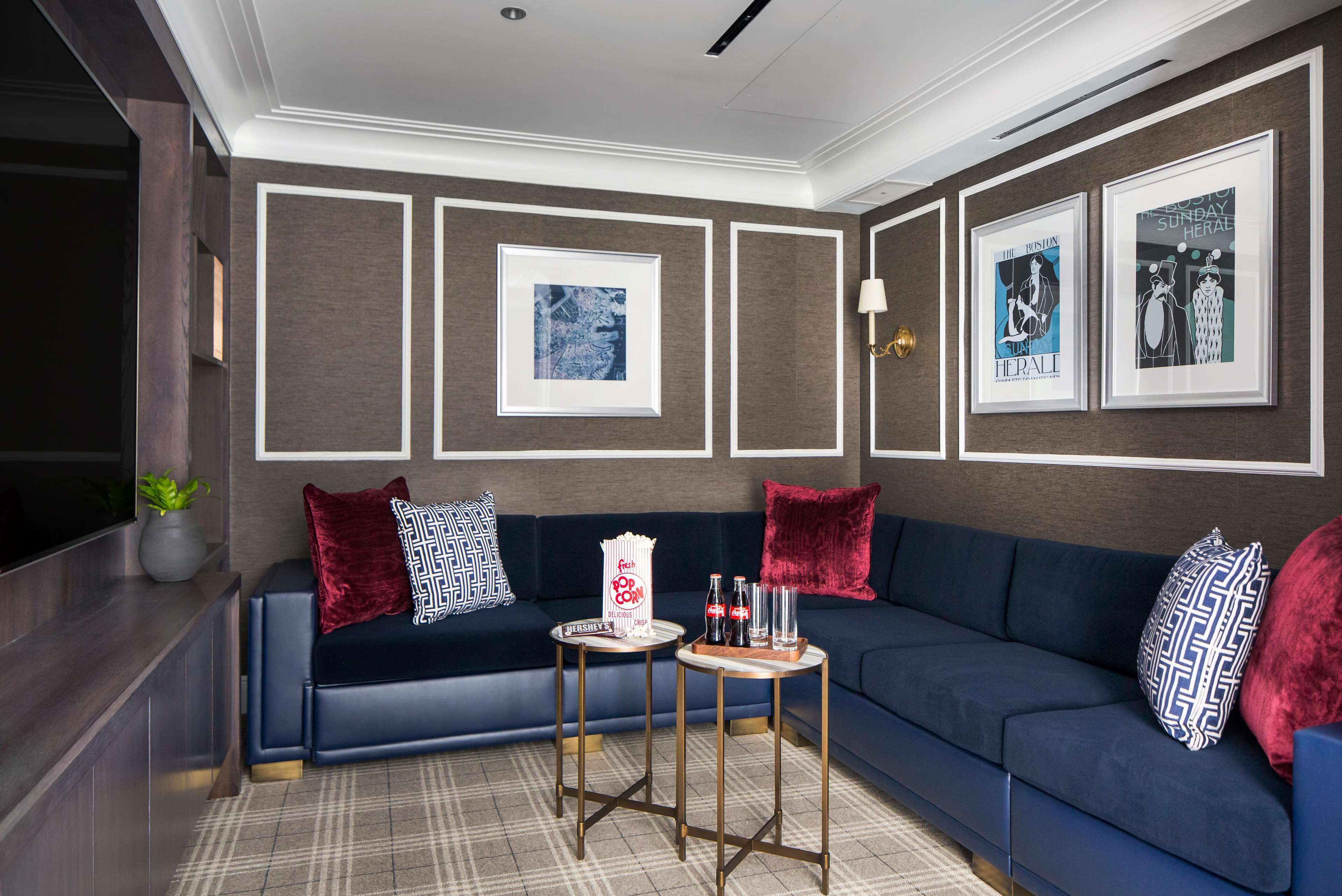 Una sala de estar moderna con un sofá azul oscuro, almohadas rojas y estampadas, una máquina para hacer palomitas y cuadros en las paredes.