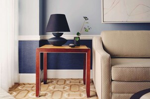 A room with a wooden side table, a black lamp, a vase with a plant, and a beige sofa.