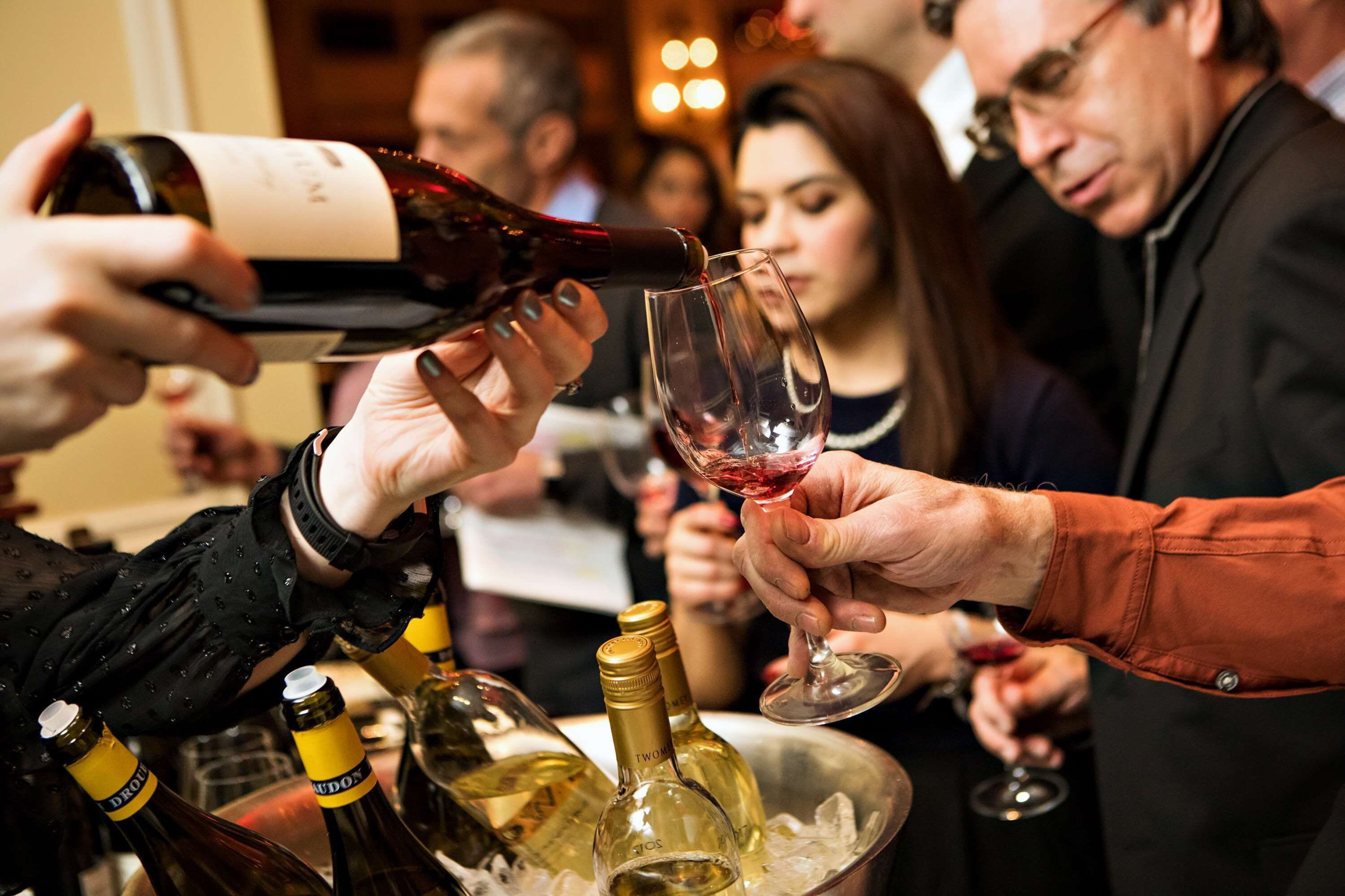 A group of people at a social event, with one person pouring wine into a glass.