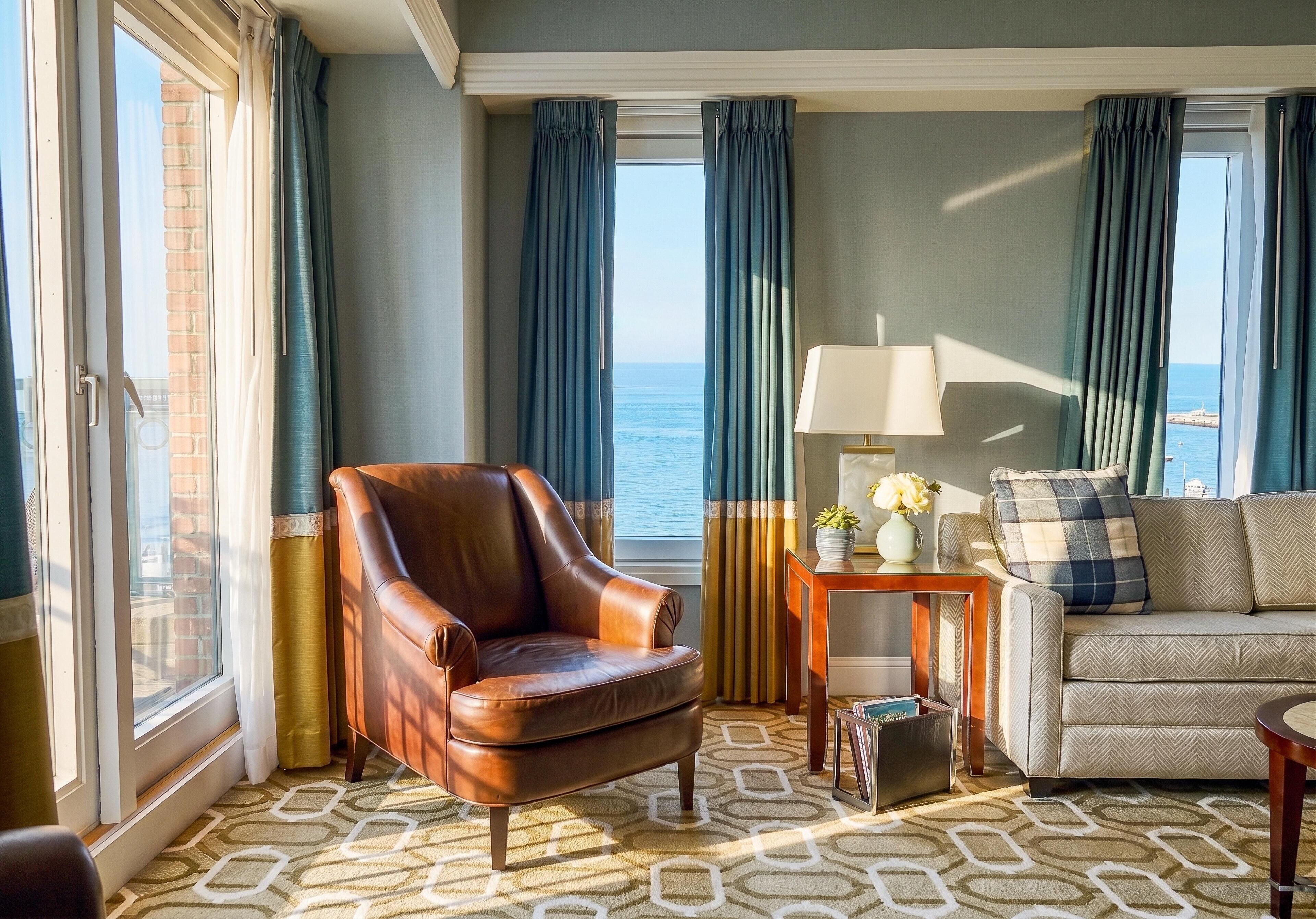 A room with a leather armchair, a sofa, a lamp, and a view of the sea.