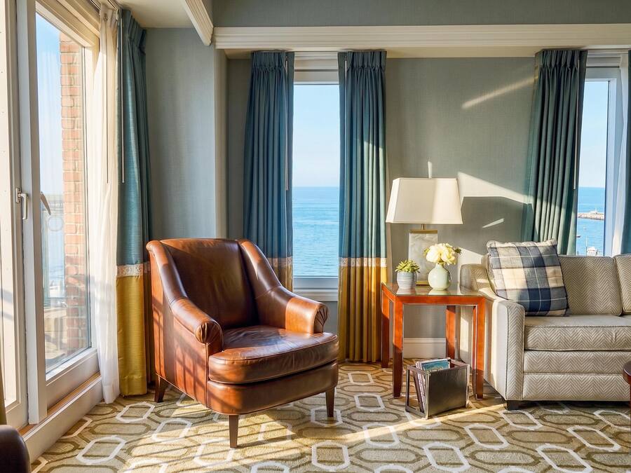 A room with a leather armchair, a sofa, a lamp, and a view of the sea.