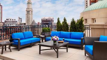 An outdoor seating area with blue sofas and a table, featuring a cityscape view in the background.