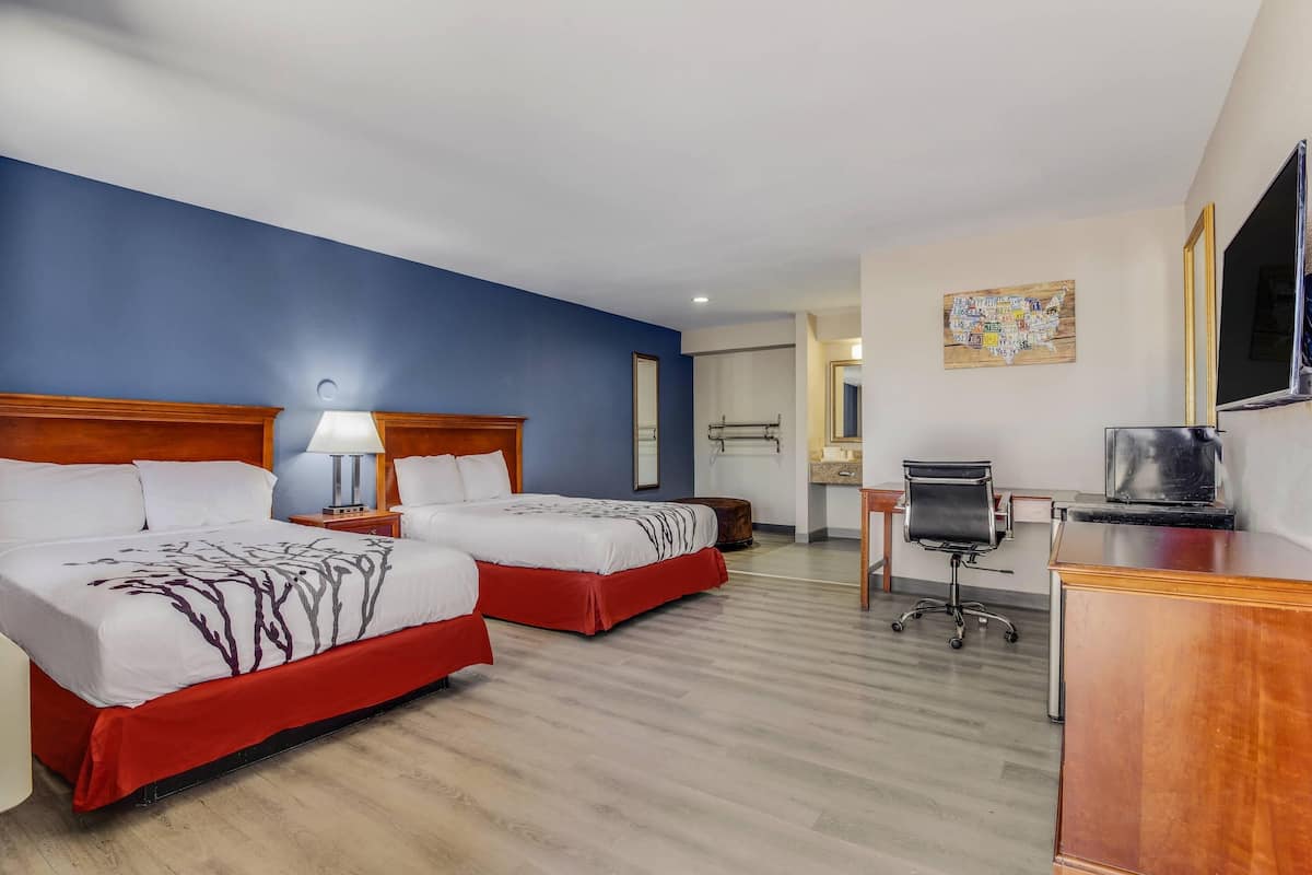 Quarto de hotel com duas camas, uma escrivaninha, uma cadeira, uma televisão e um mapa na parede.