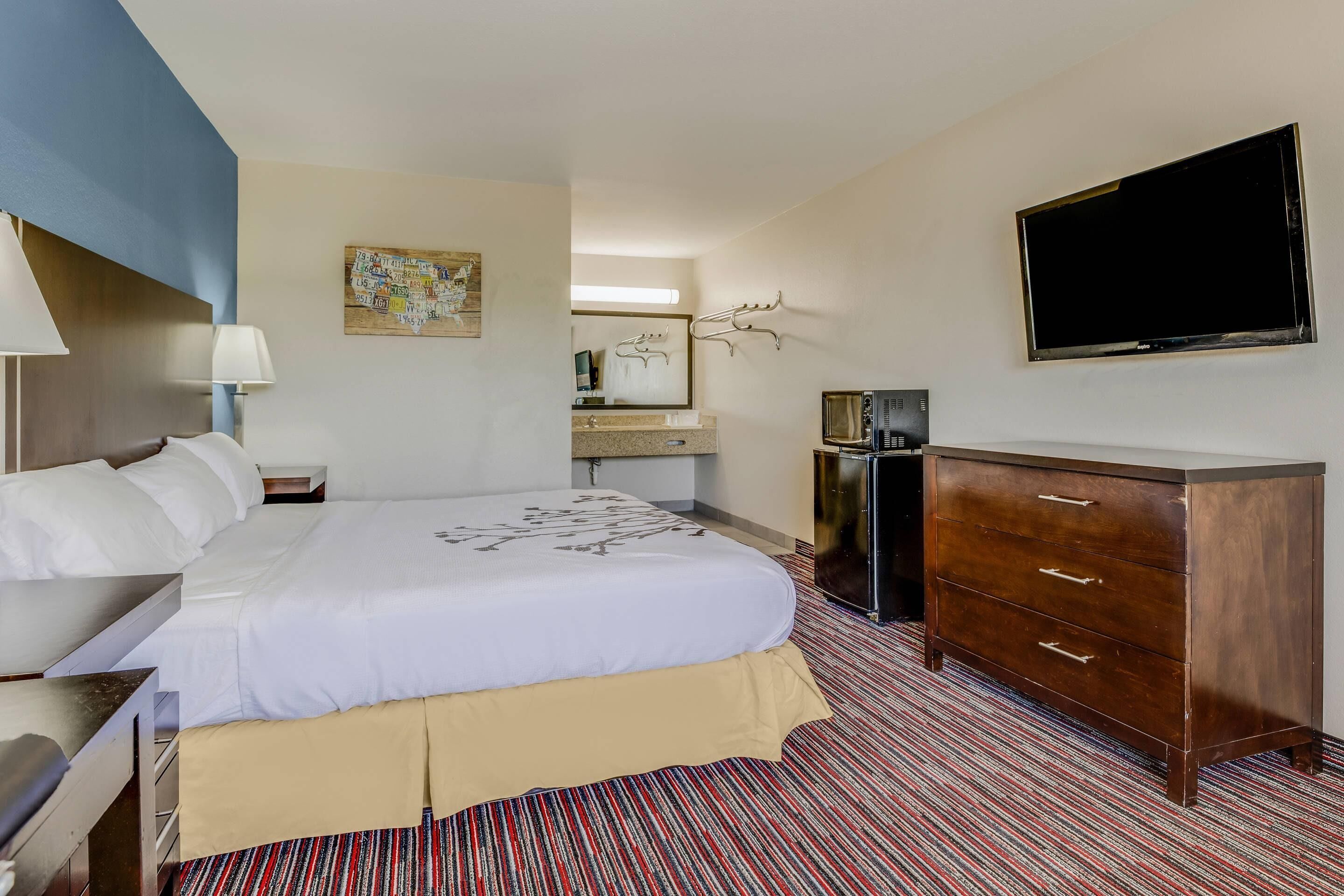 A hotel room with a bed, a dresser, a television, a desk, and a mirror.