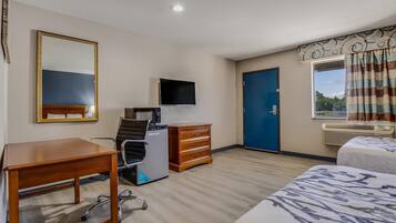 A hotel room with a desk, chair, dresser, bed, TV, and a window with curtains.