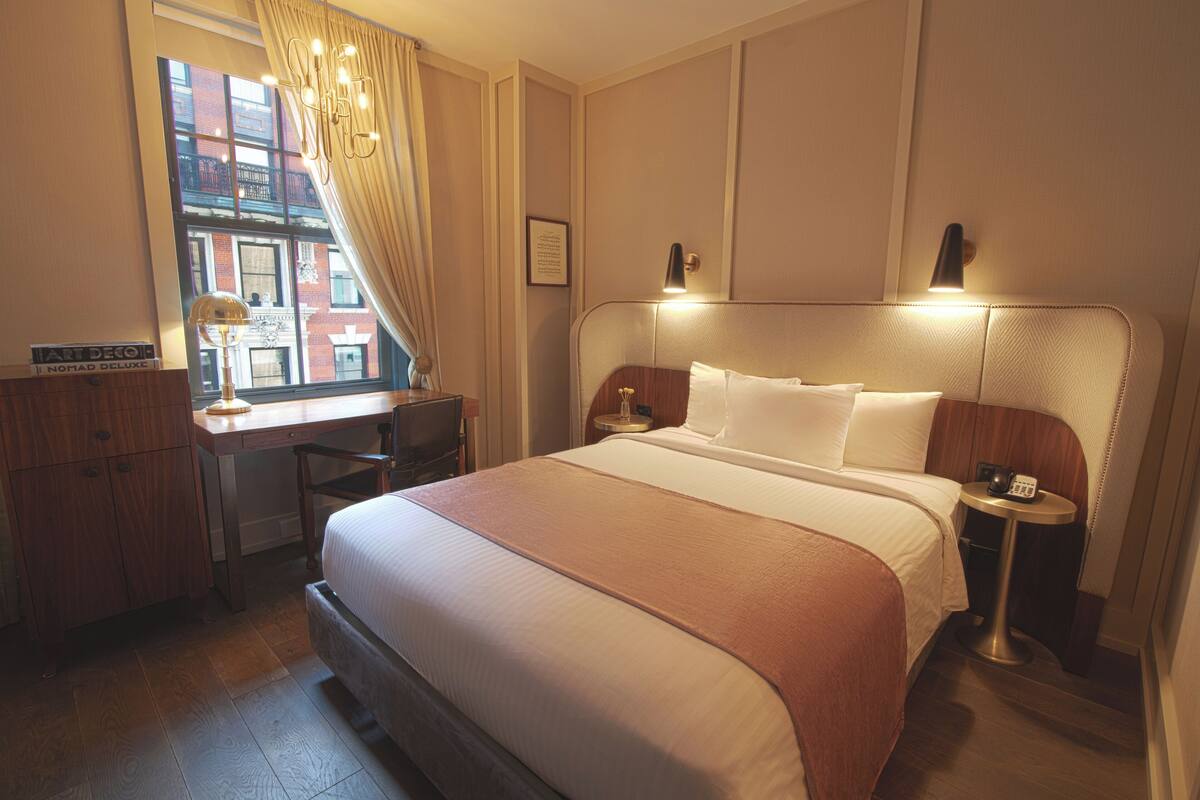 A hotel room with a large bed, a desk, a chair, a small table, and a window with curtains.