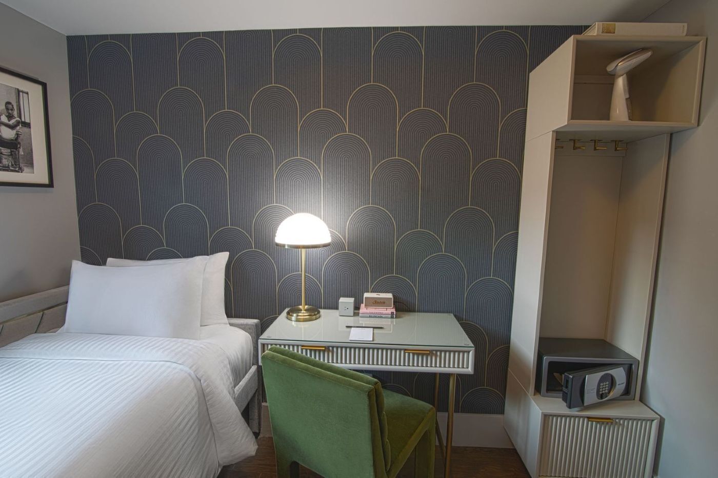 A hotel room with a bed, a desk with a lamp, a chair, a radio, and a wardrobe.