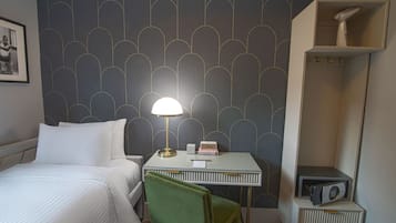 A hotel room with a bed, a desk with a lamp, a chair, a radio, and a wardrobe.