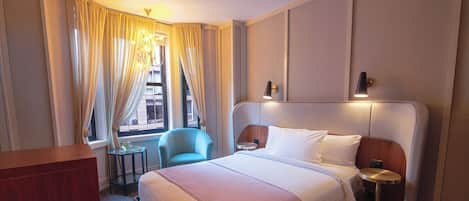 Una habitación de hotel con una cama grande, un escritorio, una silla, una mesita y una ventana con cortinas.