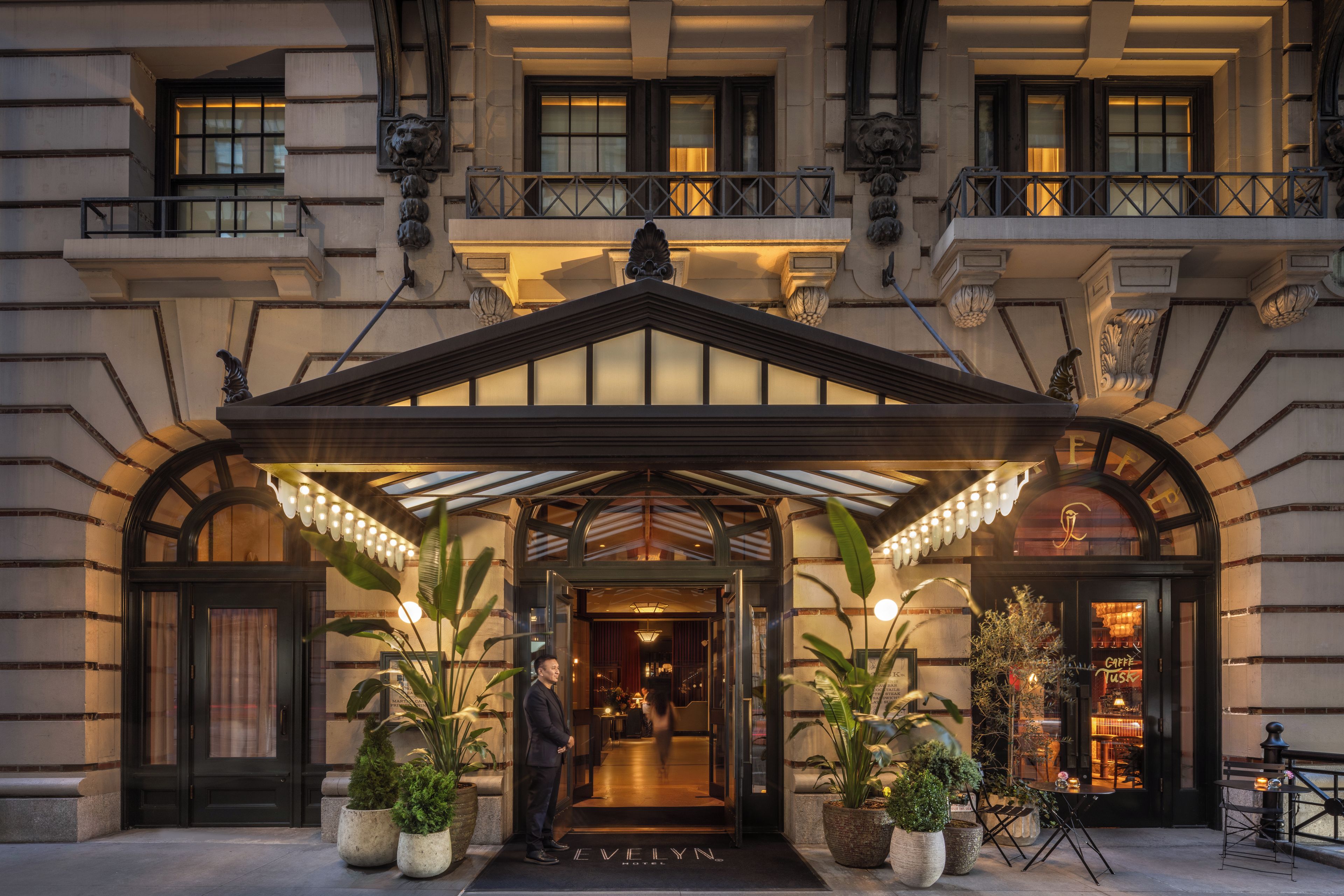 A hotel entrance with a covered entrance, potted plants, and a visible restaurant sign.