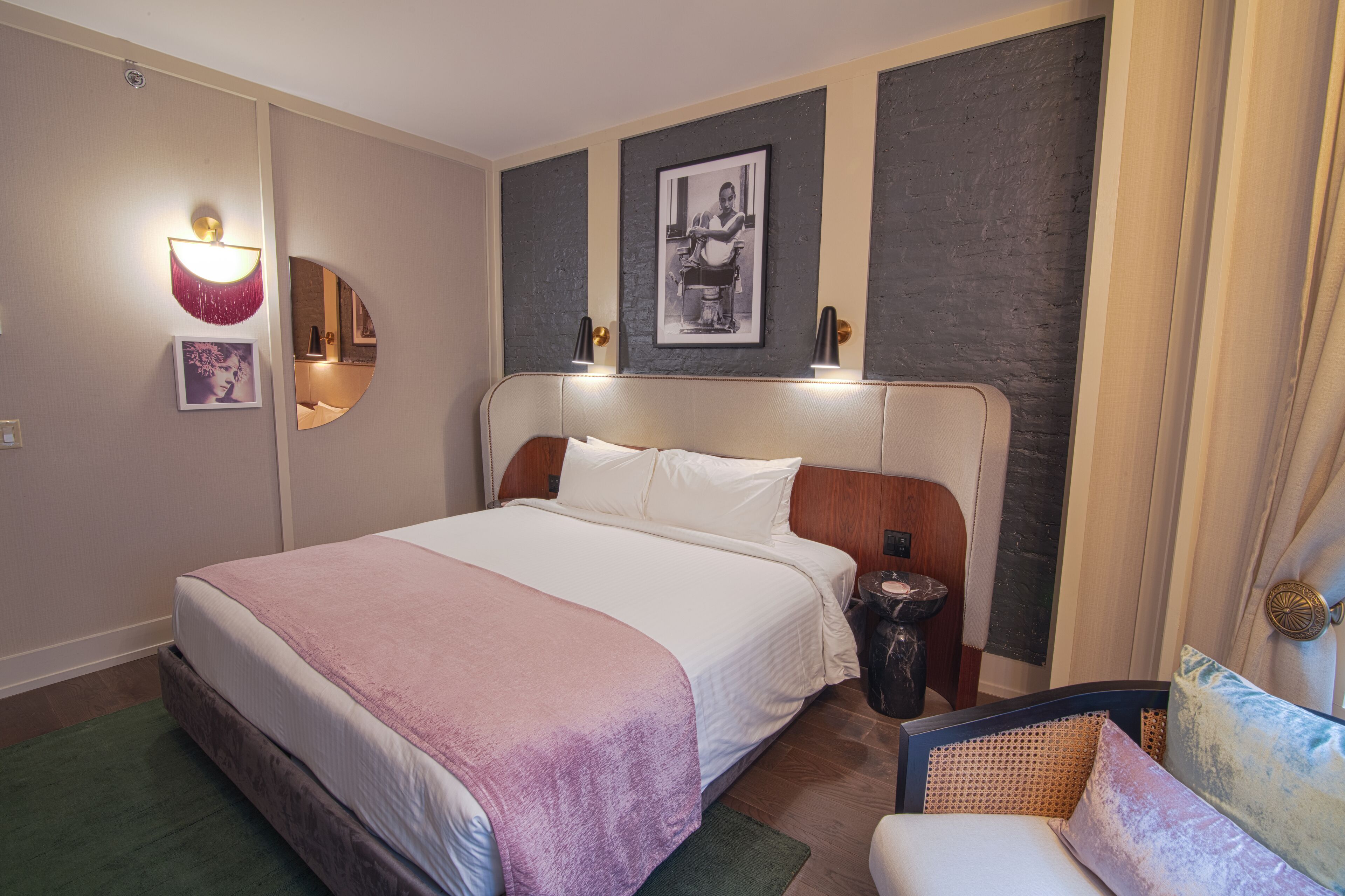Hotelkamer met een groot bed, een stoel, nachtkastje, een wandlamp en een lijst met een afbeelding.