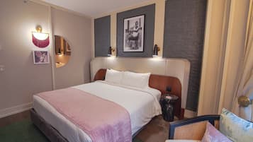 Hotelkamer met een groot bed, een stoel, nachtkastje, een wandlamp en een lijst met een afbeelding.