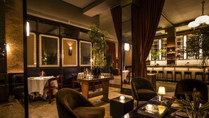 A dimly lit restaurant with a bar area, wooden furniture, and a view of the cityscape through large windows. - The Evelyn Hotel (New York)