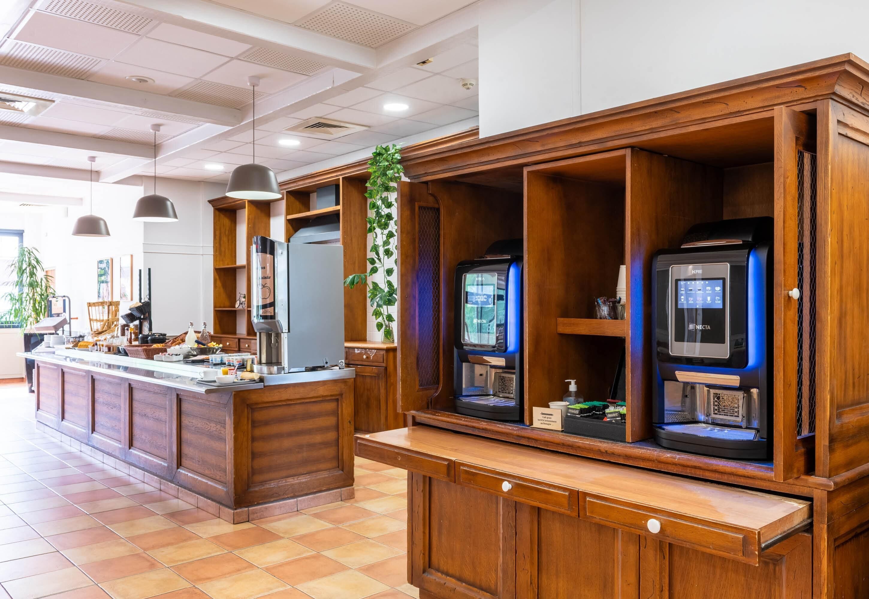 A hotel reception area with a wooden counter, a coffee machine, a microwave, and a digital display.