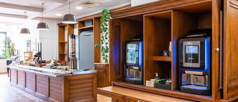 A hotel reception area with a wooden counter, a coffee machine, a microwave, and a digital display.