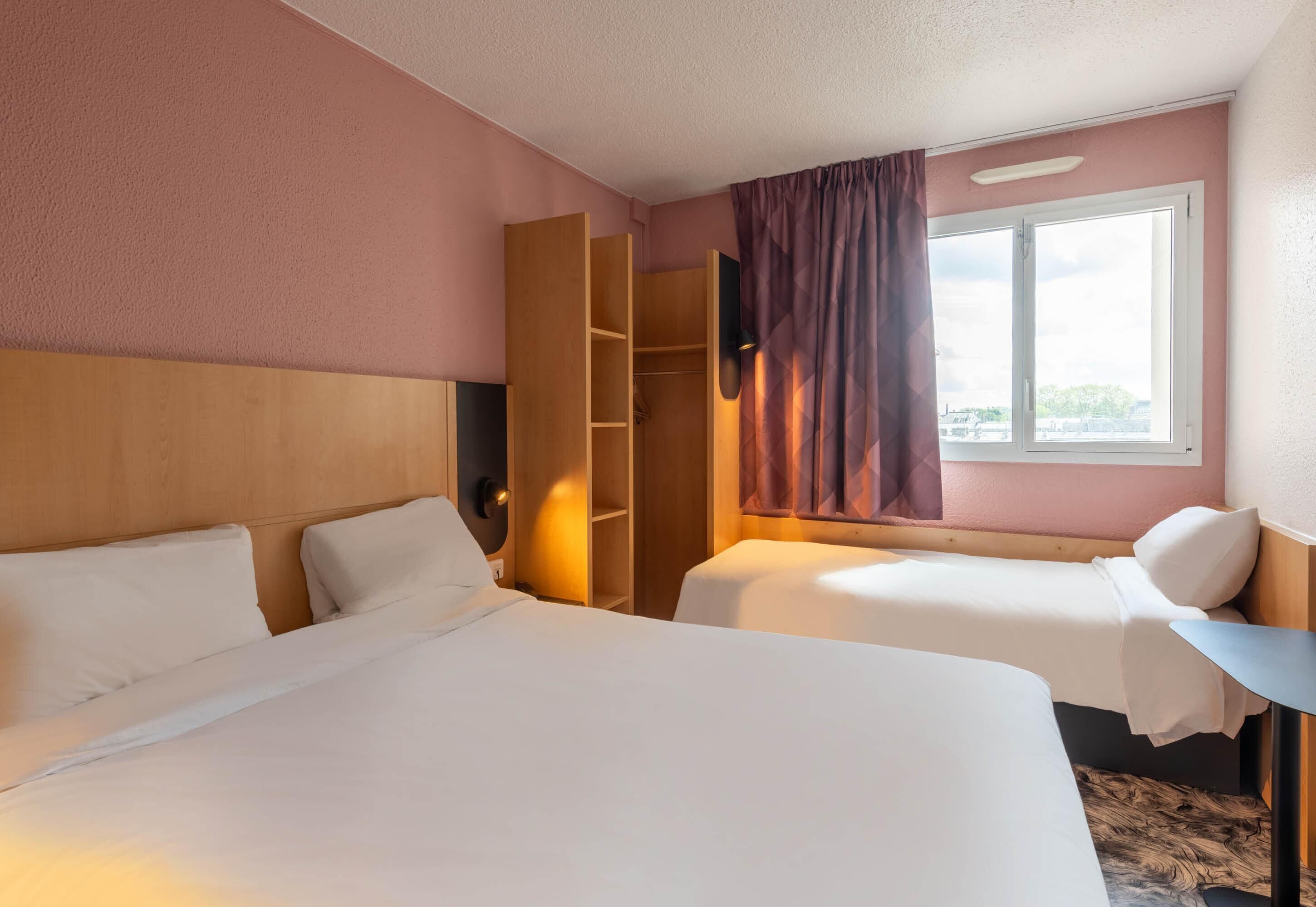 Una camera d'albergo con due letti, un armadio, una scrivania e una finestra con tende.