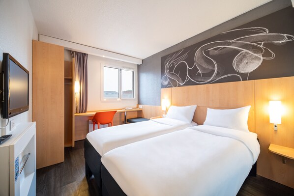Ett hotellrum med två sängar, ett skrivbord, en TV och ett stort, abstrakt konstverk på väggen.