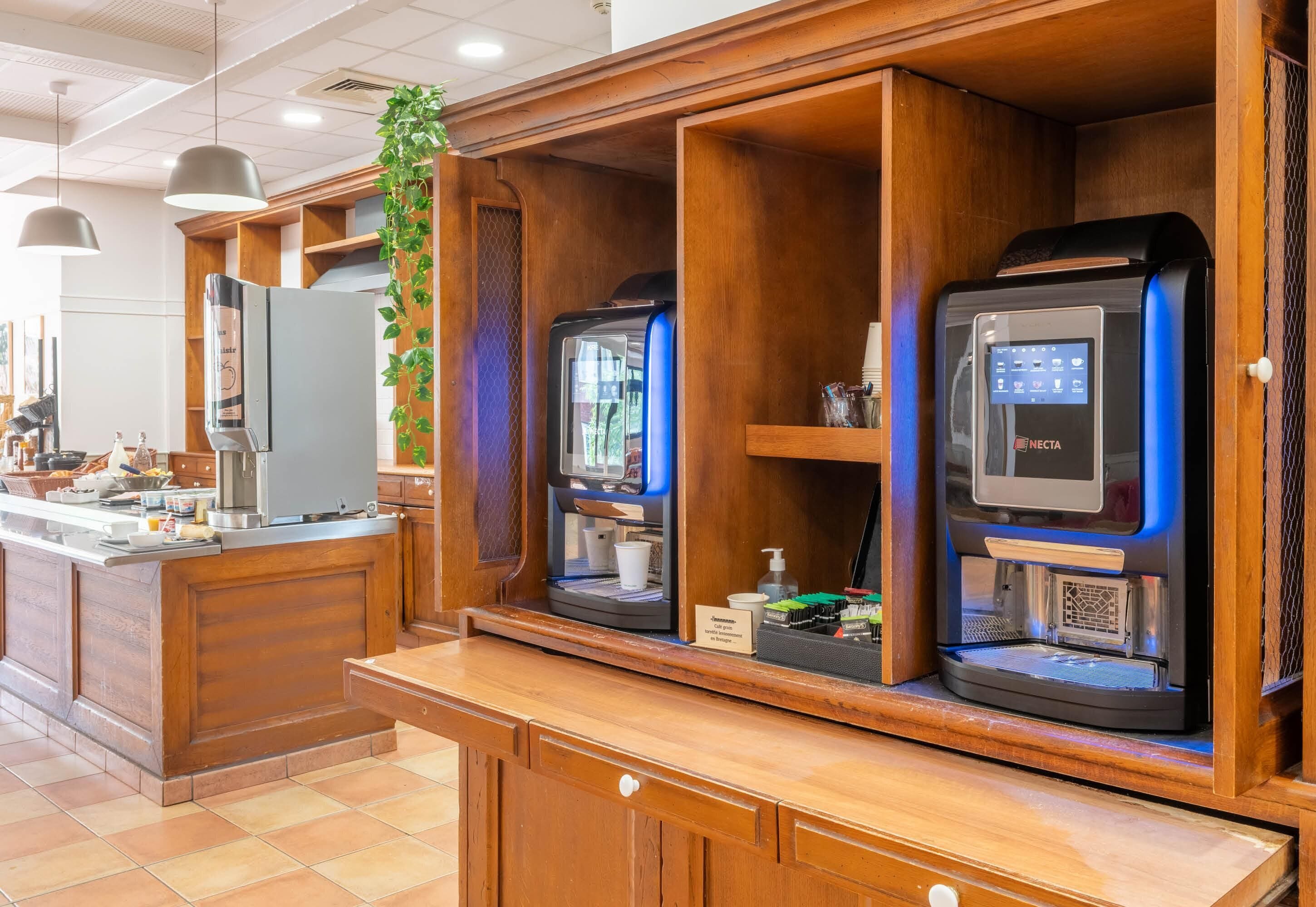 A coffee station with two espresso machines, a refrigerator, and a plant.