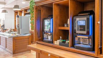 A coffee station with two espresso machines, a refrigerator, and a plant.