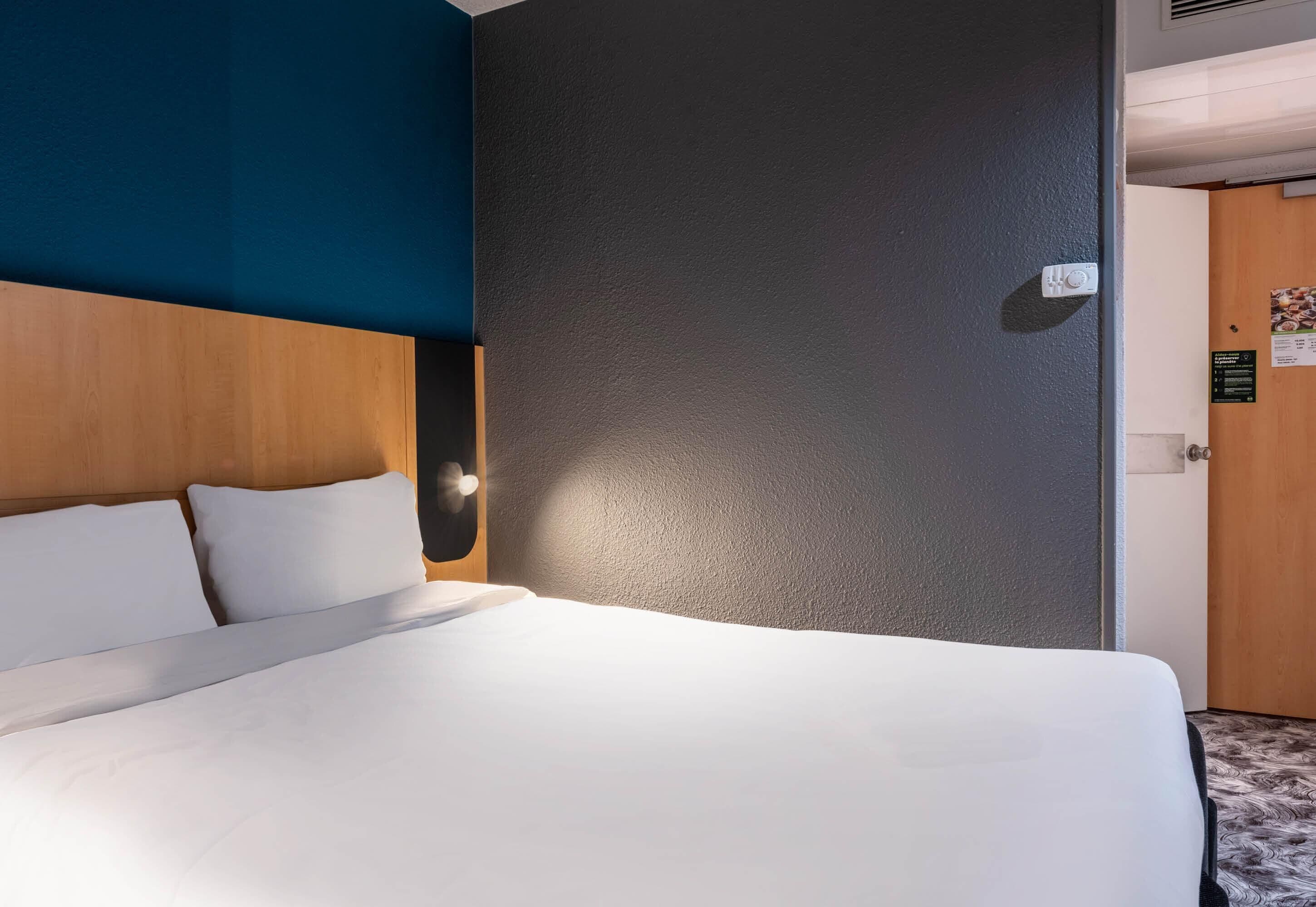 A hotel room with a bed, a wooden headboard, a dark wall, and a door.