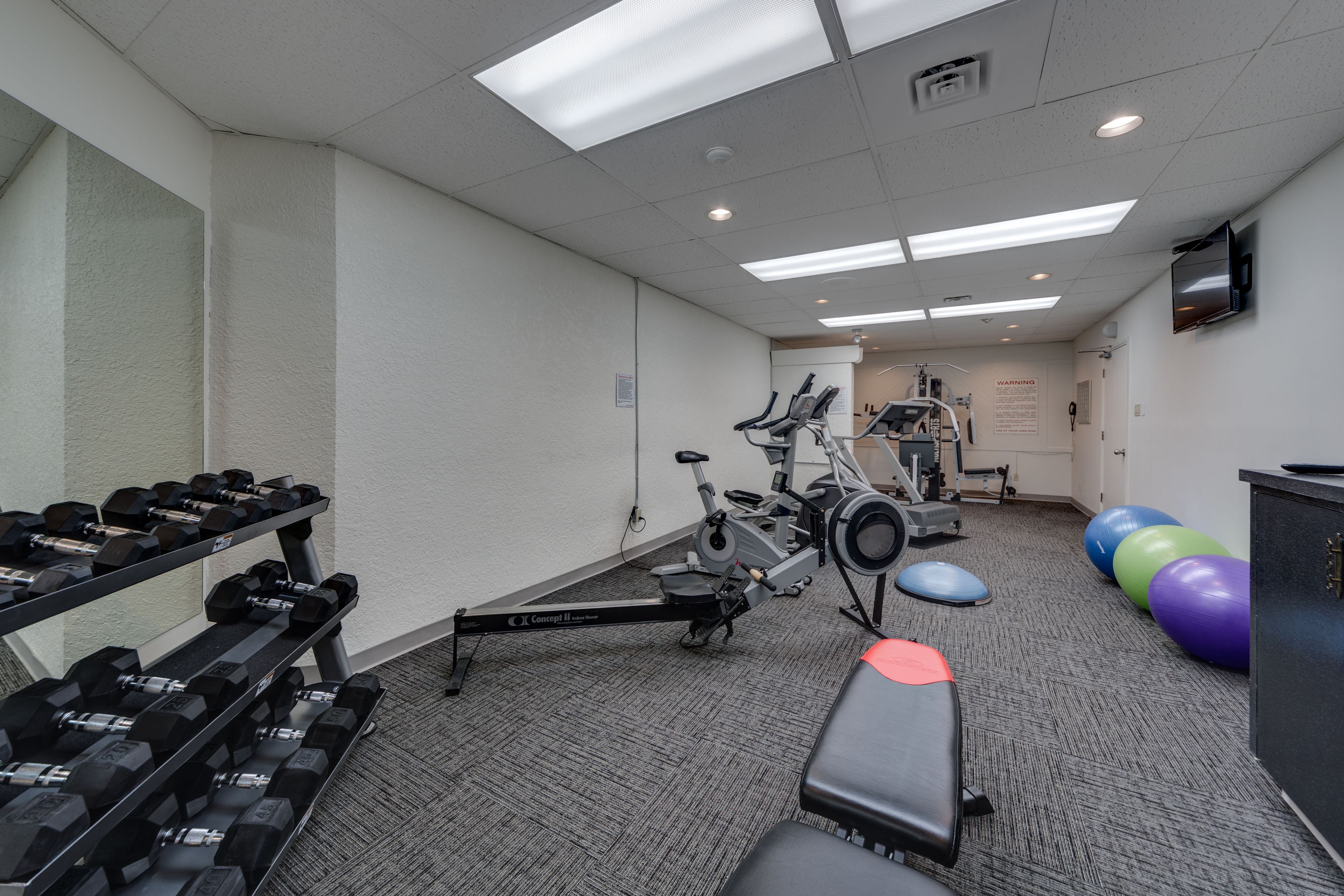 A gym with exercise equipment, including dumbbells, a stationary bike, and exercise balls.