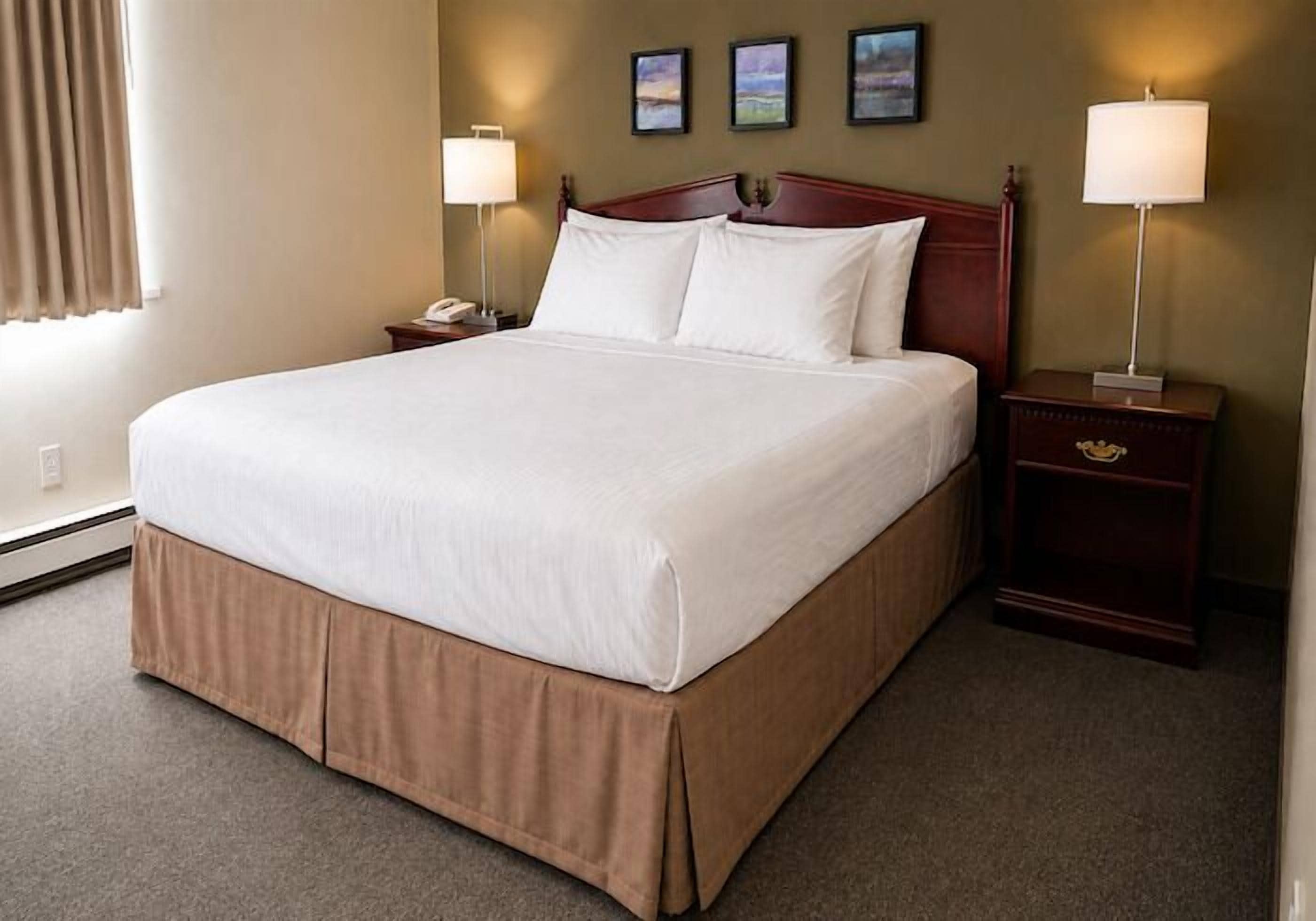 A hotel room with a large bed, two bedside tables with lamps, and a wall-mounted clock.