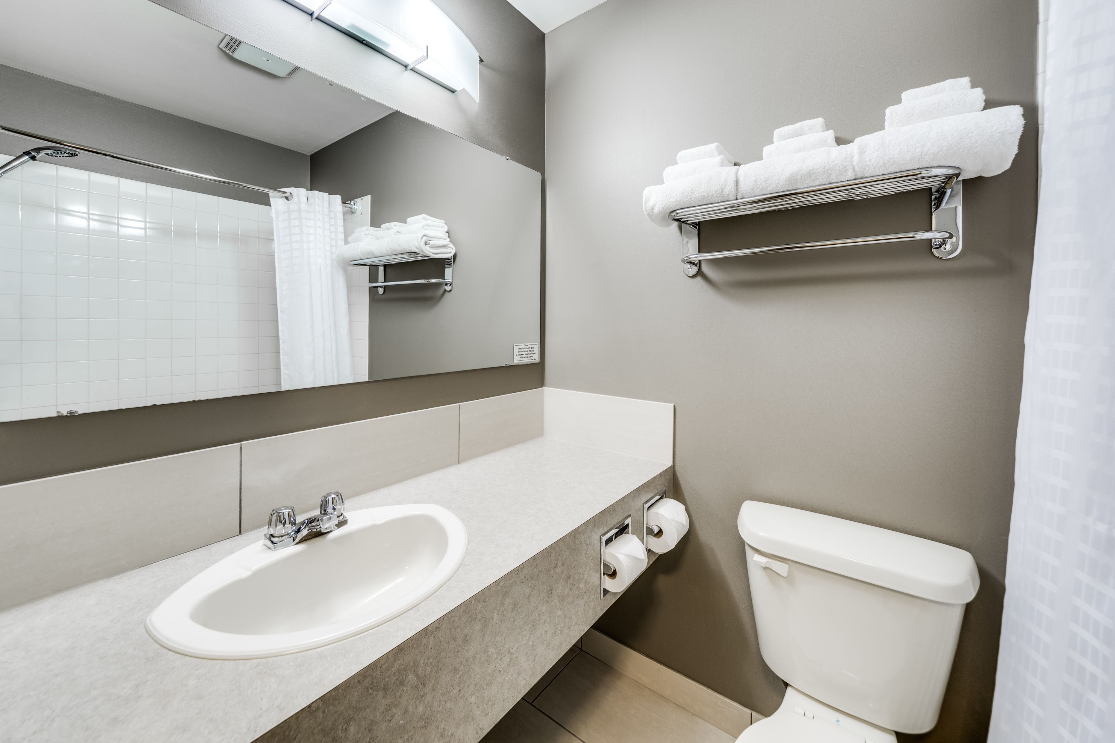 Un bagno moderno con lavandino, specchio, porta asciugamani e water.
