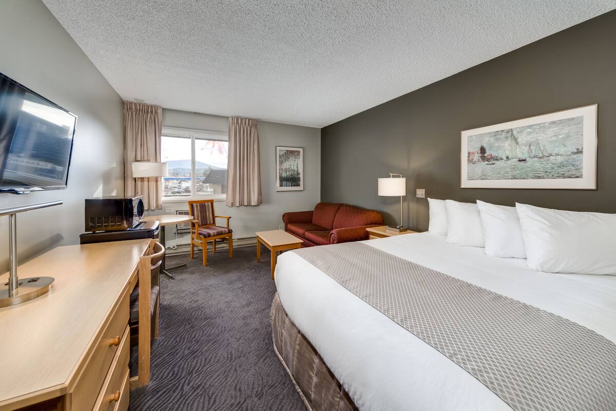 Quarto de hotel com cama, escrivaninha com computador, cadeira, sofá e televisão.
