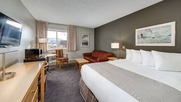 Une chambre d’hôtel équipée d’un lit, d’un bureau avec un ordinateur, d’une chaise, d’un canapé et d’une télévision.