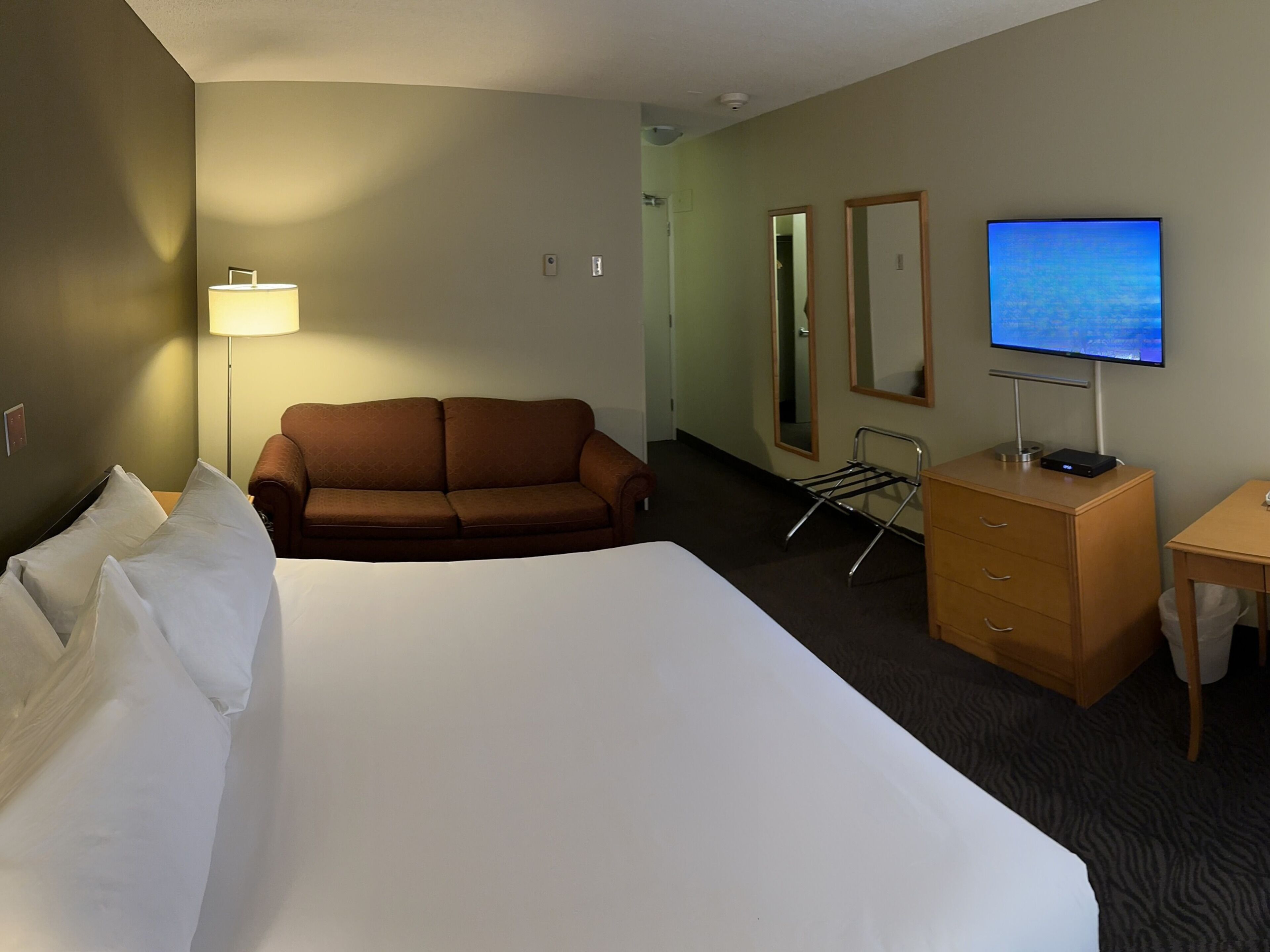 Une chambre d’hôtel avec un grand lit, un canapé marron, un bureau avec une télévision, une lampe et un miroir.