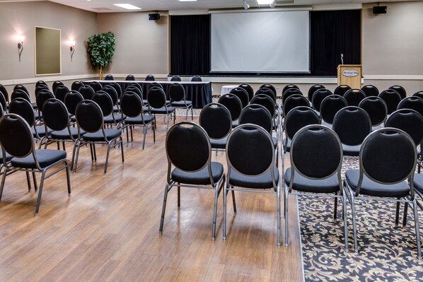Un salón de conferencias con filas de sillas, un atril y una pantalla para proyector.