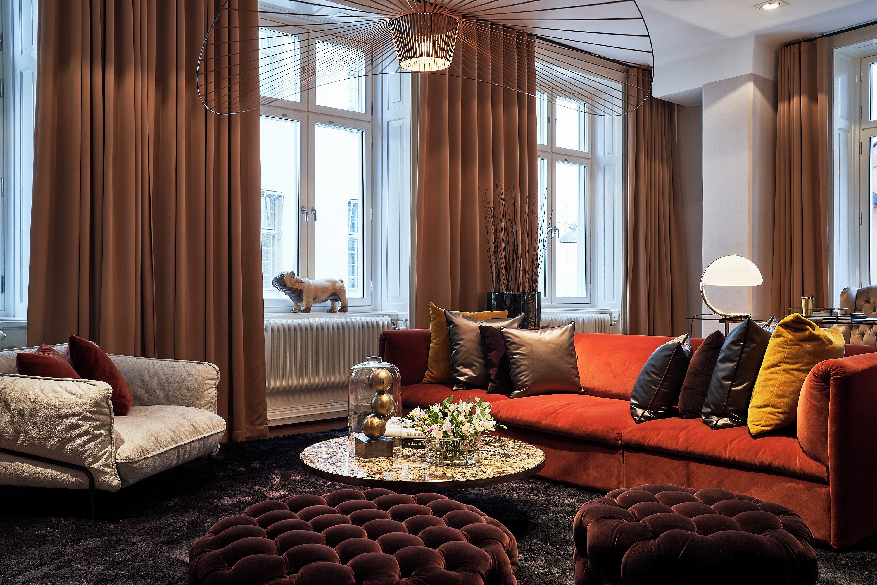 Un salon avec un canapé rouge, un fauteuil blanc et une table basse ronde agrémentée d’objets décoratifs.